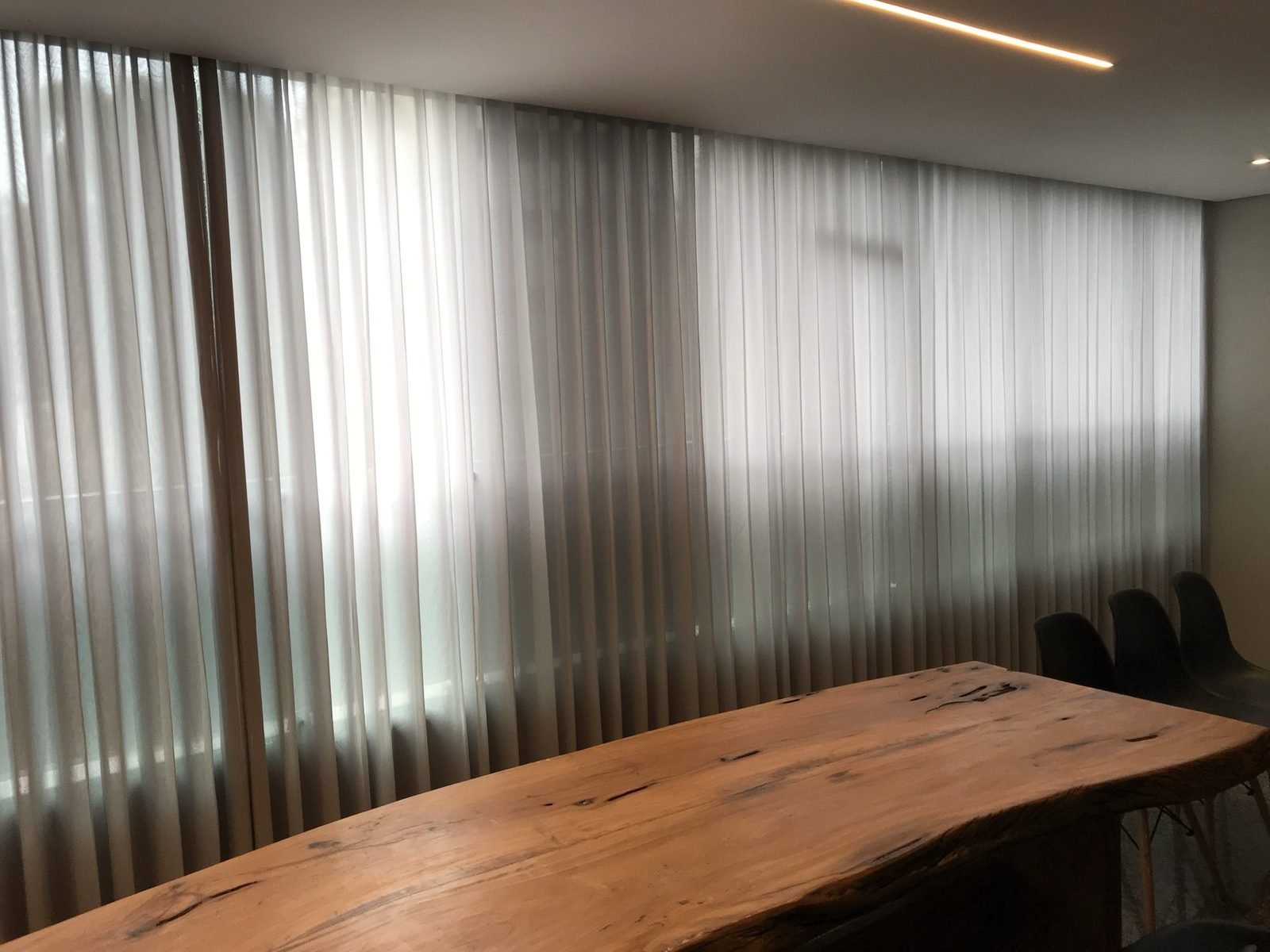 Sala de jantar com mesa de madeira maciça e cortina wave translúcida filtrando a luz